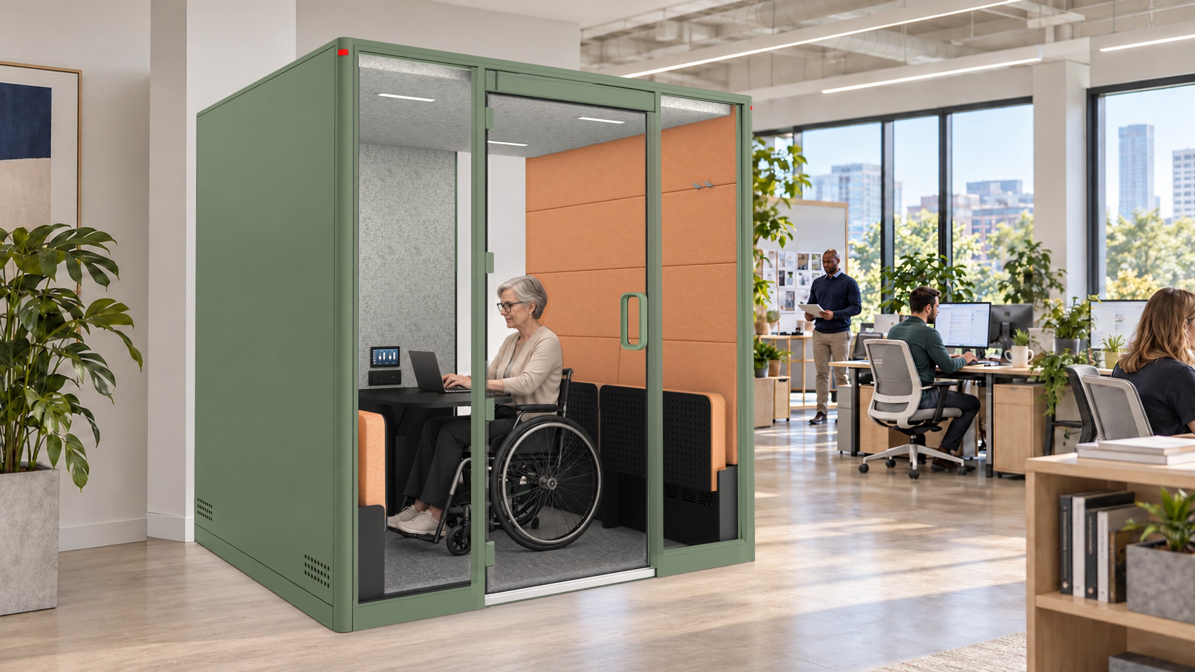 A Calma For All pod, a grey-haired woman in a wheelchair working at the desk inside, colleagues at their desks around it