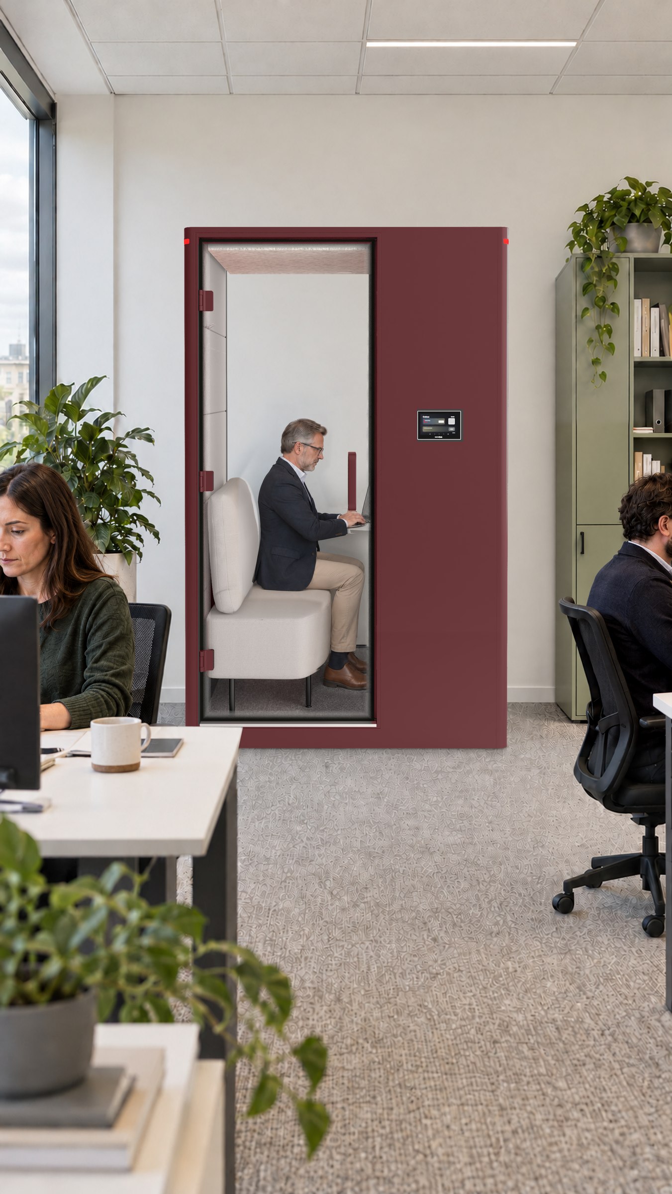 A Calma For U pod in a consultancy, a grey-haired man on a video call inside, a colleague at her desk in front